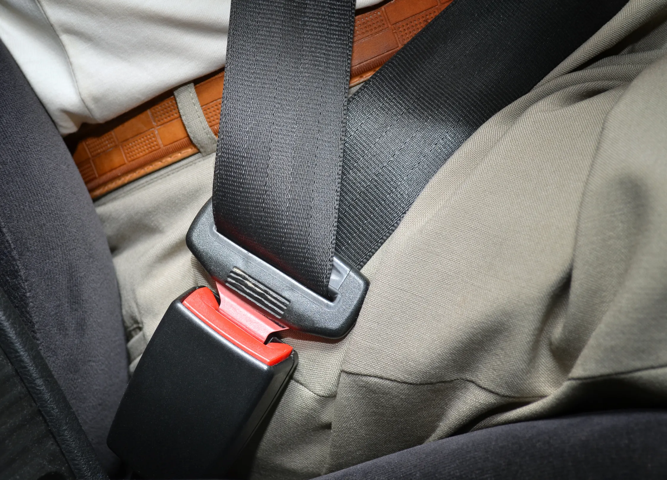 A fastened seat belt routed across an occupant's lap and hip, with the tongue plate engaged in the buckle beside the seat cushion.